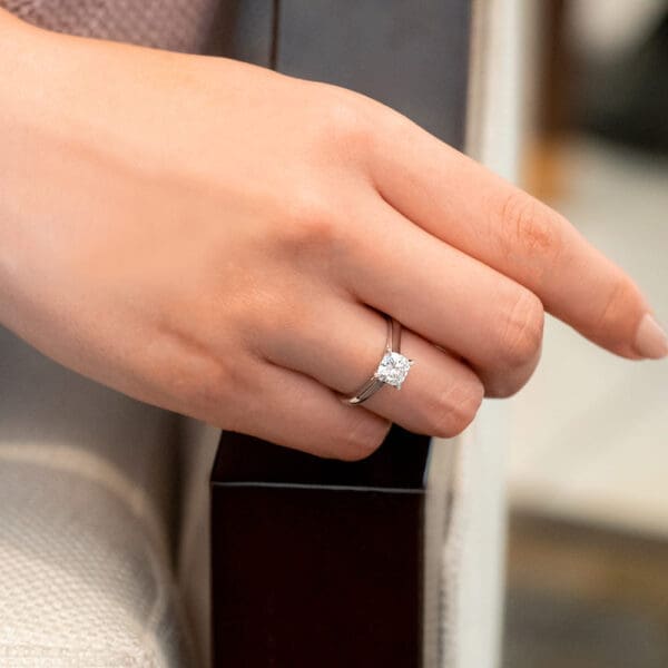 Model Wears Leisel Cushion 6.0 White Gold Moissanite 4 Prong Crossover Gallery Solitaire Band Ring