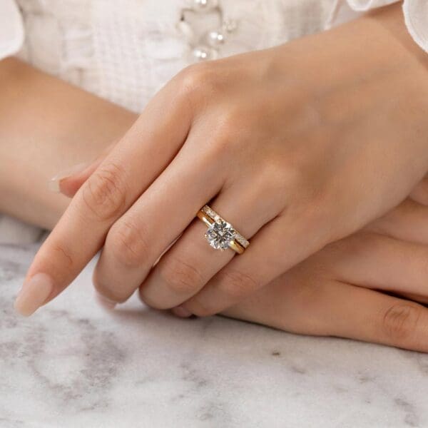 Model Wears Angela 2.0 Yellow Gold Diamond Half Set U Prong Wedding Band Fiona Round 8.5 Moissanite 4 Prong Solitaire Ring