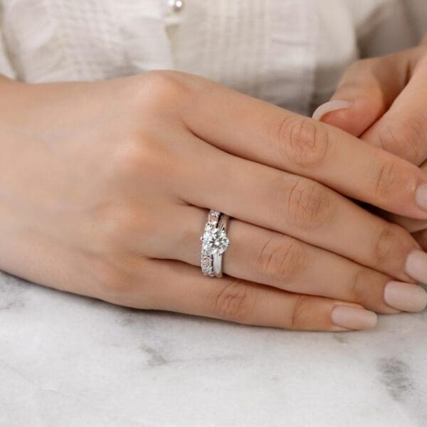 Model Wears Angelica 3.0 White Gold Alternating Pink Diamond U Prong Set Wedding Band Audrey 7.5 Moissanite Solitaire Ring