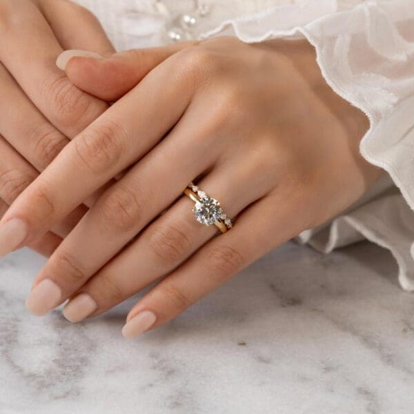 Model Wears Evie Yellow Gold Diamond Marquise Round Shared Prong Band Fiona Round 8.5 Moissanite 4 Prong Solitaire Ring