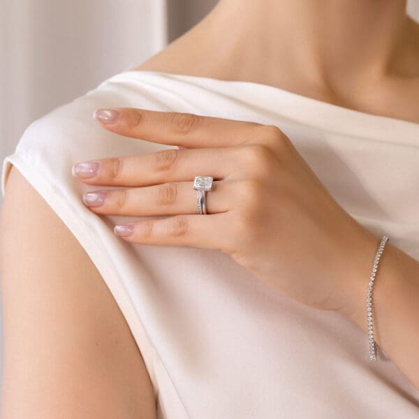Model Wears Millie 1.1 White Gold Moissanite Pave Set Wedding Band Hattie Emerald 9X7 Under Rail Bridge Stone Set Ring
