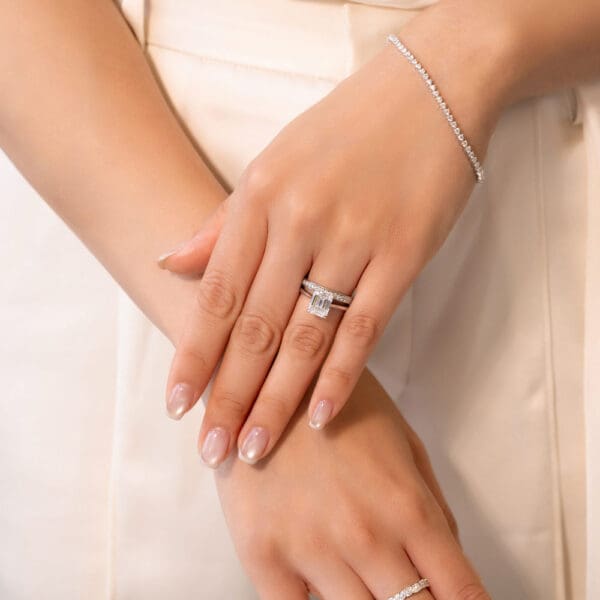Model Wears Millie 1.5 White Gold Moissanite Pave Set Wedding Band Hattie Emerald 9X7 Stone Set Under Rail Bridge Ring