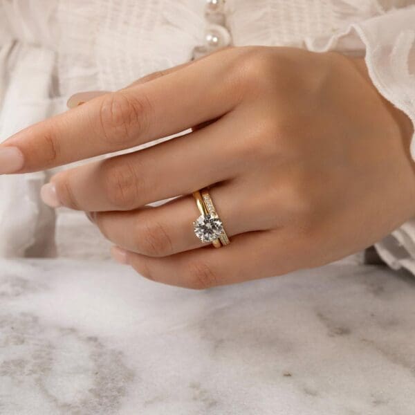 Model Wears Millie 1.5 Yellow Gold Diamond Pave Set Wedding Band Fiona Round 8.5 Moissanite 4 Prong Solitaire Ring