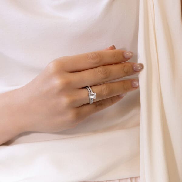 Model Wears Platinum White Gold Moissanite Angela 1.5 U Prong Set Band Odette 8X6 Emerald Interlocking Toi Et Moi Ring