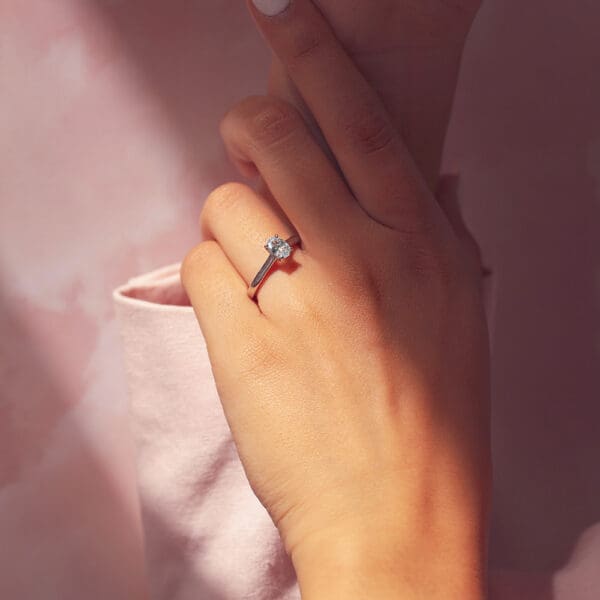 Model Wears Leisel Oval 7X5 Front White Gold Moissanite 4 Prong Crossover Gallery Solitaire Band Ring 2