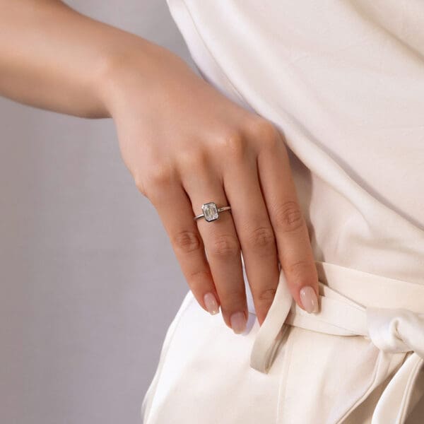 Model Wears Lottie Emerald 8X6 White Gold Moissanite Bezel Rounded Band Solitaire Ring