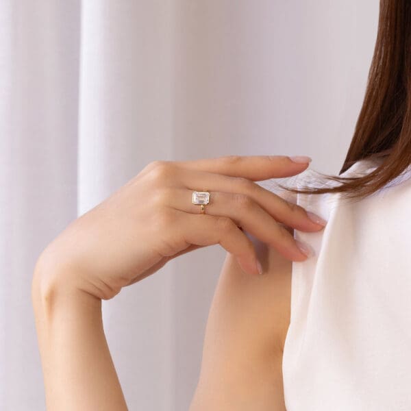 Model Wears Lottie Emerald 9X7 Yellow Gold Moissanite Bezel Rounded Band Solitaire Ring