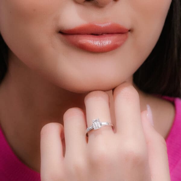 Model Wears Debbie Emerald 7X5 White Gold Moissanite Tapered Side Stones Prong Set Trilogy Ring