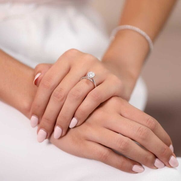 Model Wears Hattie Oval 9X7 White Gold Moissanite 4 Prong Accented Under Rail Bridge Tapered Engagement Ring